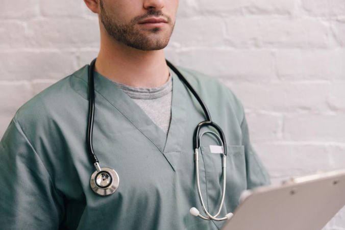 Health care professional in scrubs, with notepad and stethoscope